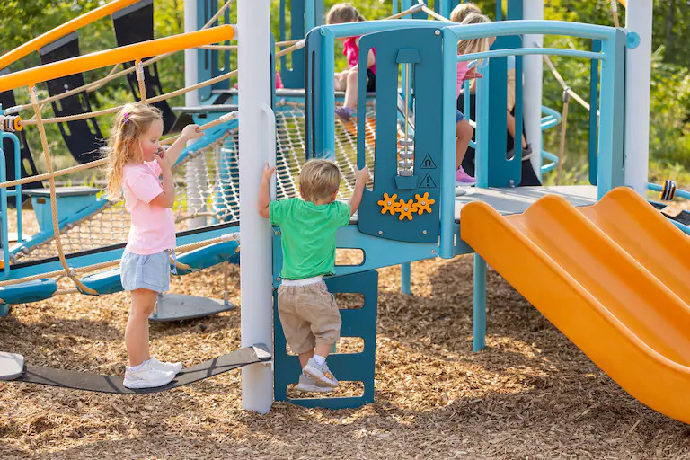Two children climbing on blue and orange Volo Pico+ playground.